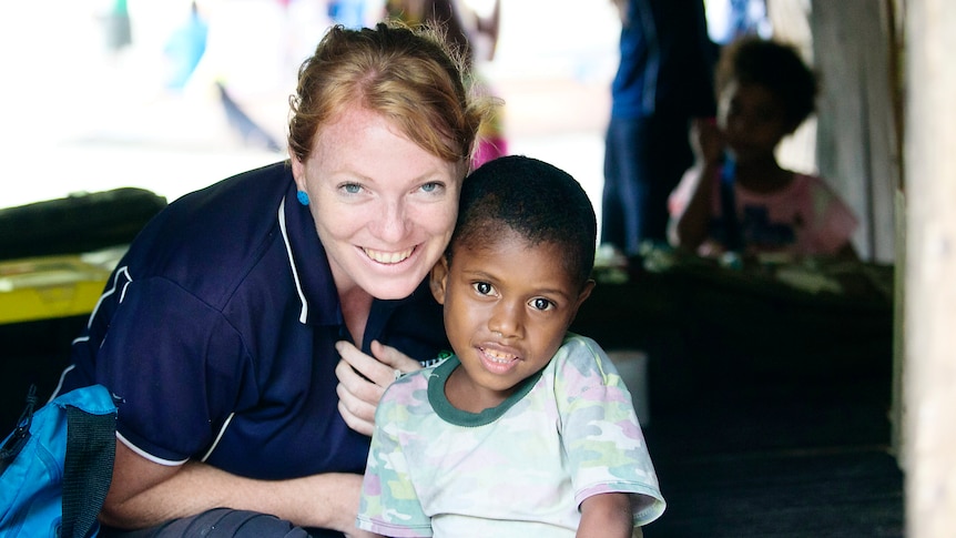 A woman wearing a navy T-shirt smiling next to a small boy from the local PNG community