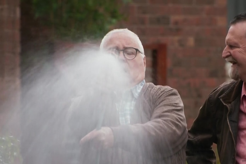 a man holds a hose spraying water. another man looks at him.