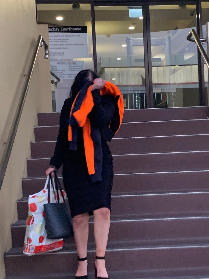 Black-haired woman uses a hi-vis jumper held up to her face as she walks down the courthouse steps.