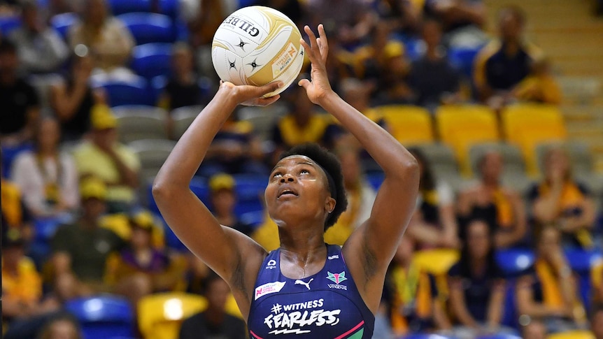 Mwai Kumwenda shoots for goal holding a netball above her head in both hands and looking up