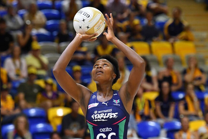 Mwai Kumwenda shoots for goal holding a netball above her head in both hands and looking up