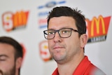 Josh Carr wears North Adelaide colours and glasses. He speaks at a press conference.