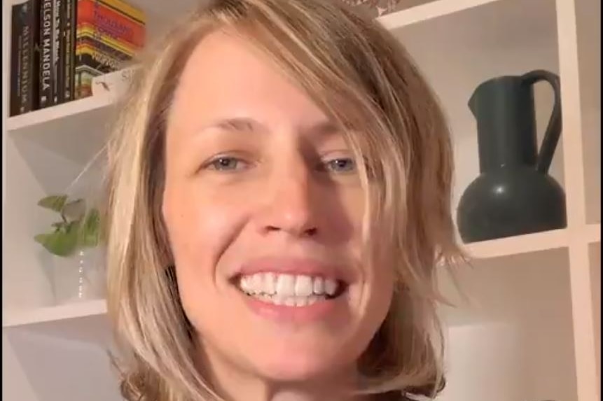 A woman wearing a black shirt smiles while standing in front of a bookshelf.