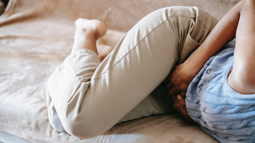 Woman curled up with hands over abdomen