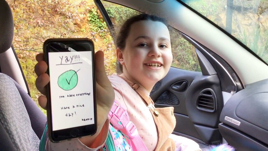 A young girl holds a phone which reads 'yay! you have everything' on the screen