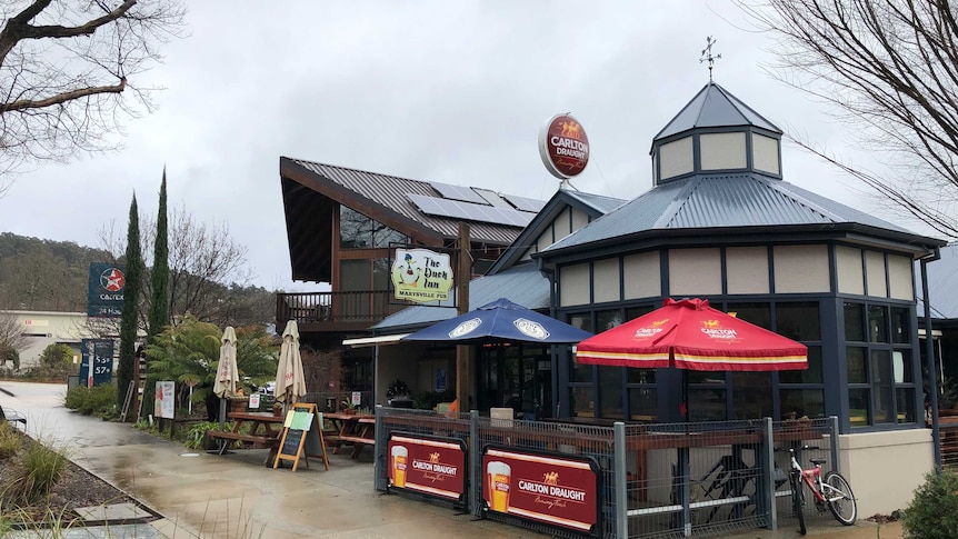 The exterior of the Duck Inn pub, with chairs and umbrellas outside on a cloudy day.