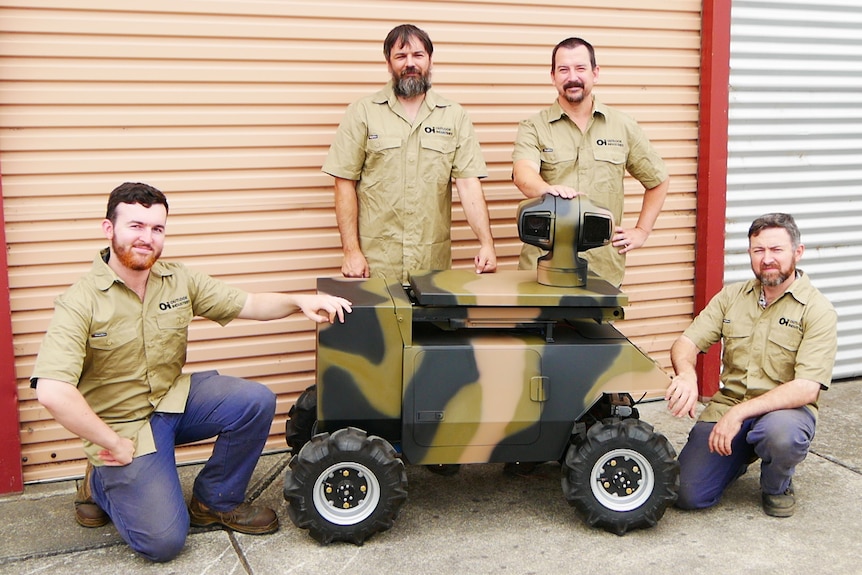 Four men in khaki shirts standing around a small robot which looks like a big remote control car