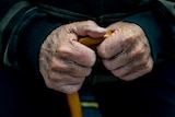 A close up of an elderly man's hands as they hold a walking stick