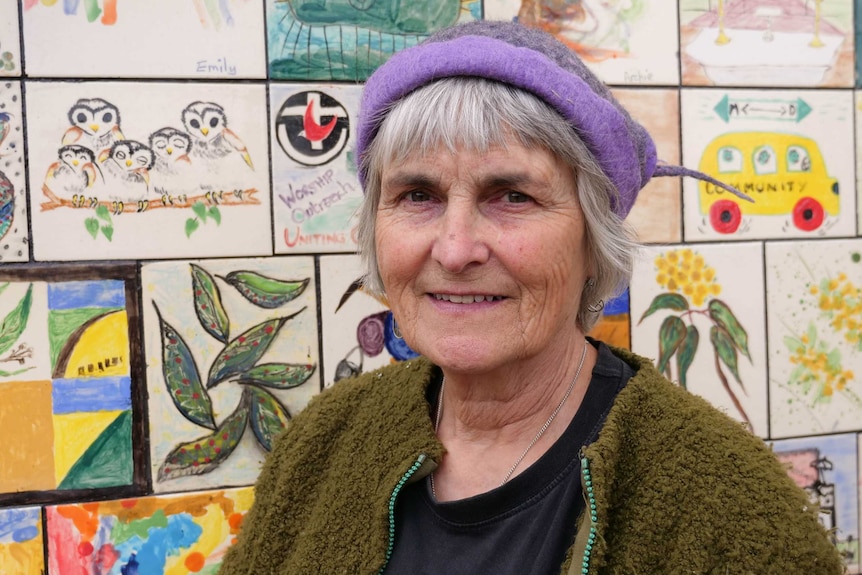 A women with a purple hate stands in front of a wall of hand-painted tiles