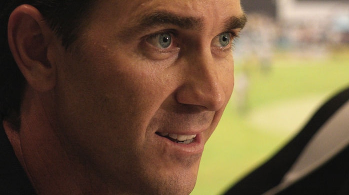 A close up shot of Justin Langer with a cricket pitch in the background.