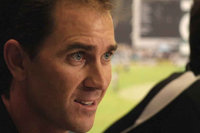 A close up shot of Justin Langer with a cricket pitch in the background.