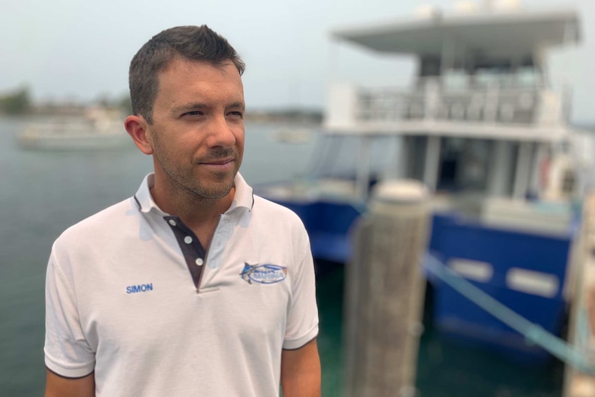 A man in a white t-shirt with an out of focus boat in the background.