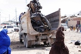 People look on as a truck takes away the twisted, burnt out remains of a car used in a bomb attack in Somalia