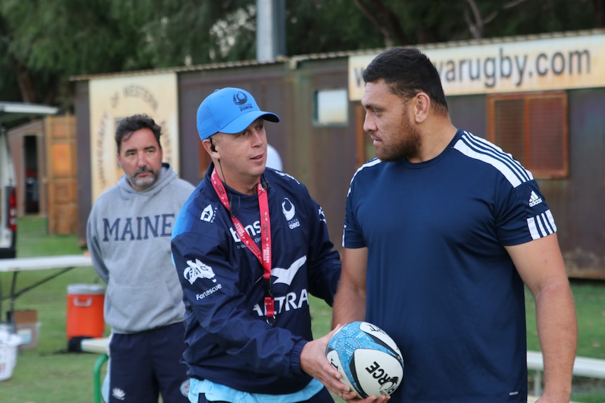 A rugby union coach hands a ball to a player