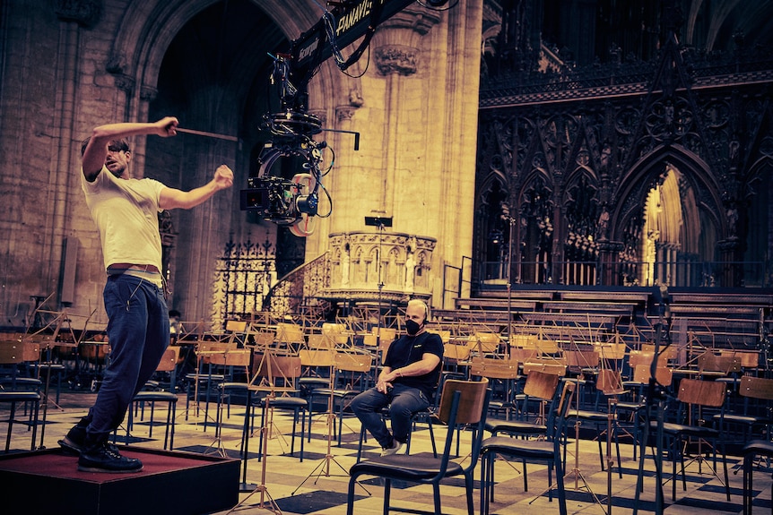 Bradley Cooper practices conducting at Ely Cathedral under the watchful eye of a seated Yannick Nézet-Séguin.