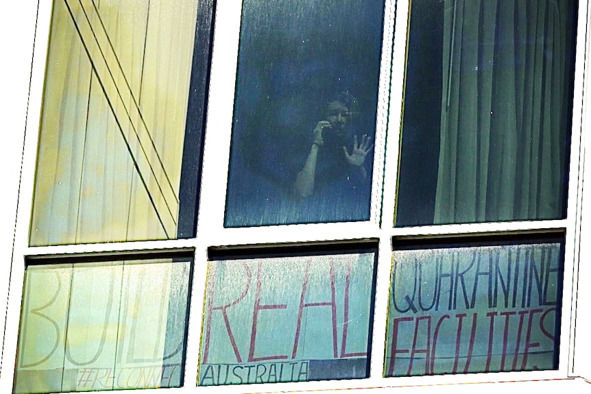 Rikki-Lee Romeyn at hotel quarantine window with sign saying: Build real quarantine facilities