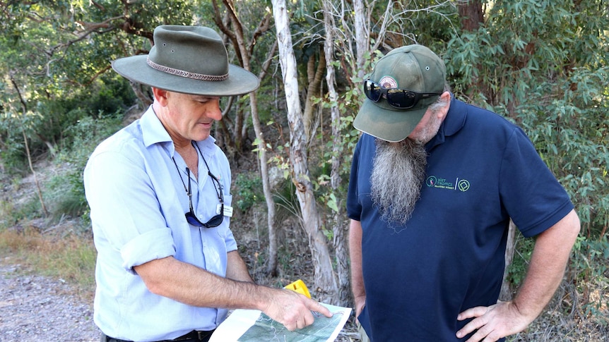 Two men stand together looking at a map.