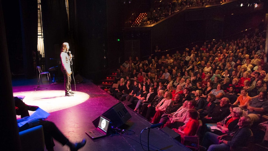 A man in a spotlight performs onstage to a crowd.