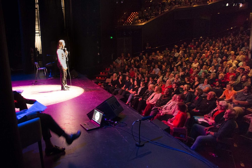 A man in a spotlight performs onstage to a crowd.