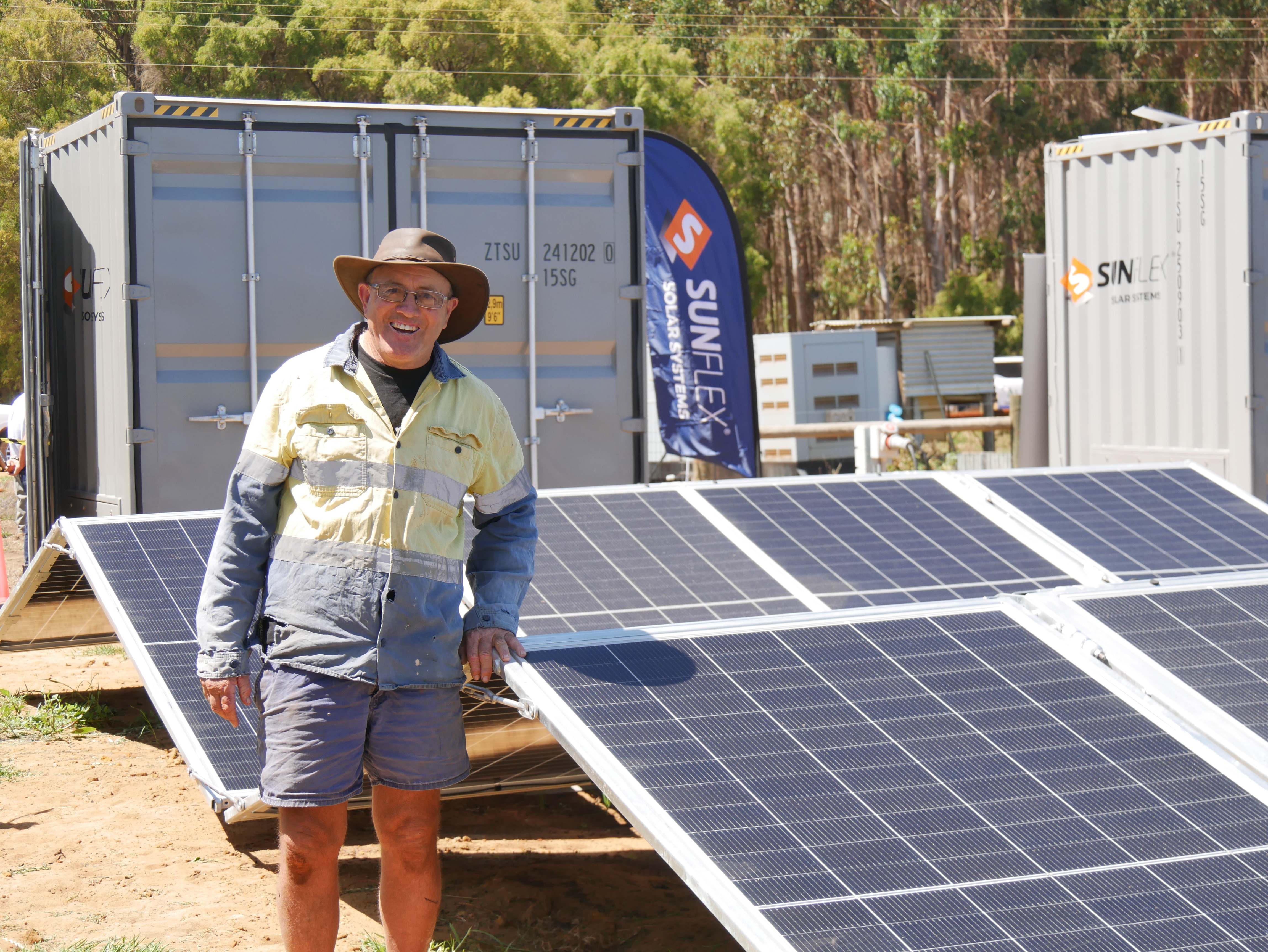 Man in long-sleeved shirt standing next to solar panels.