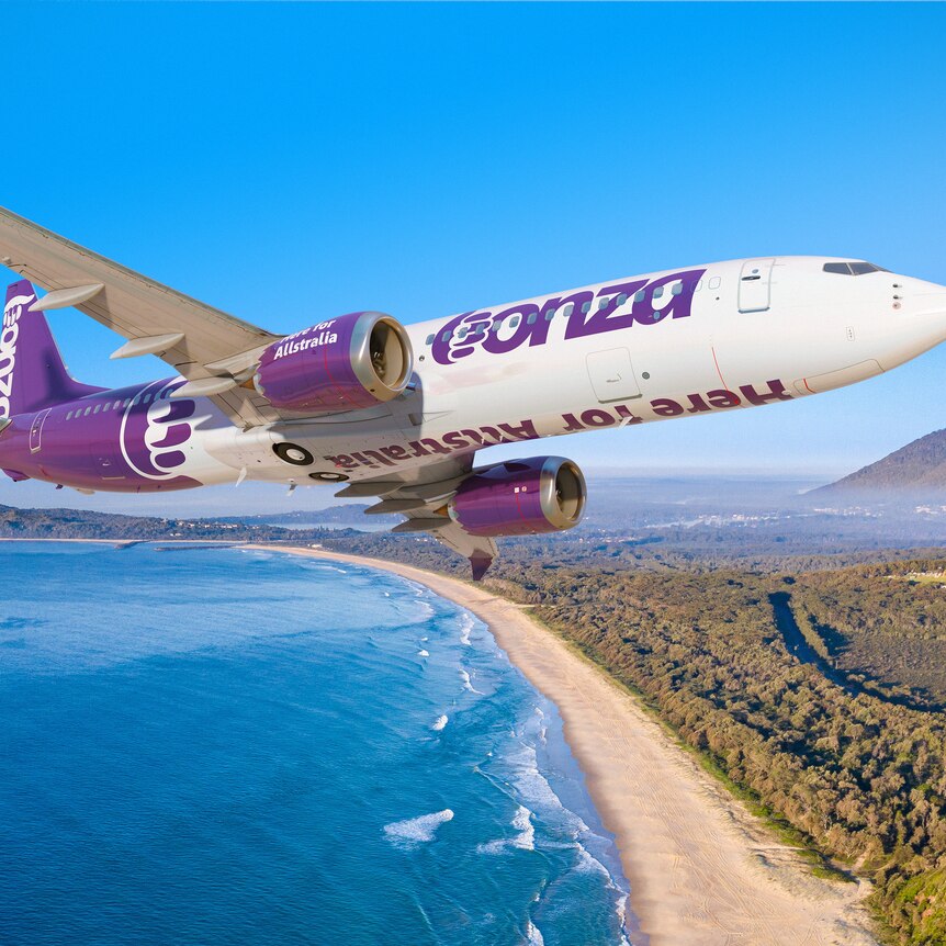 An in-flight picture of an airliner over a beach, the plane in purple and white livery showing the word "Bonza".