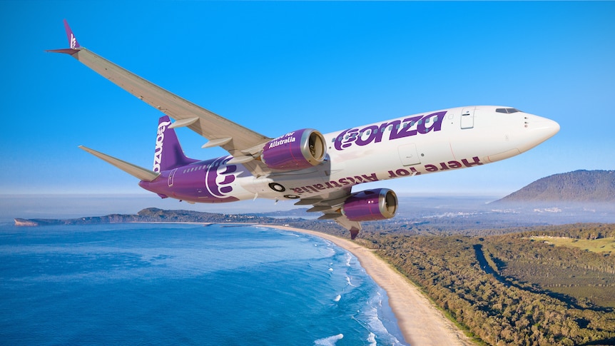 An in-flight picture of an airliner over a beach, the plane in purple and white livery showing the word "Bonza".