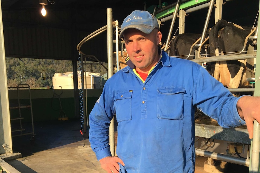 Farmer Luke Bloomfield leans against shed on dairy farm.