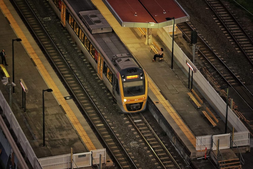 Looking down at train and commuters wait at platform at South Brisbane railway station.