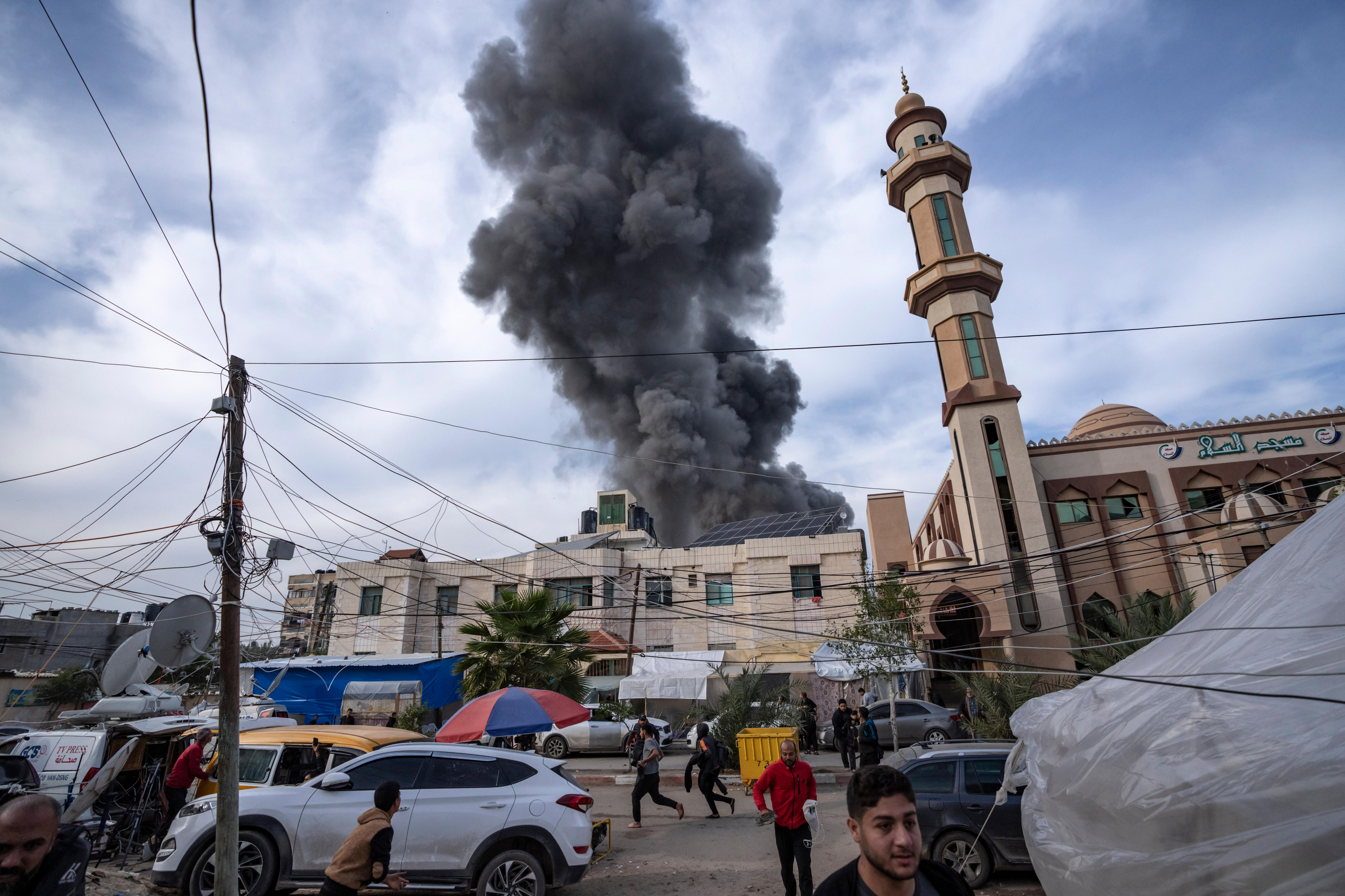 Smoke rises from a building with a mosque in the foreground. 