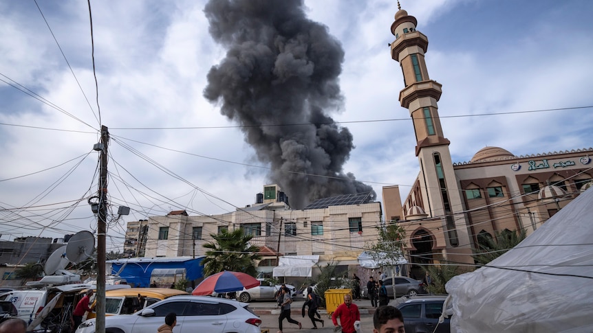 Smoke rises from a building with a mosque in the foreground. 