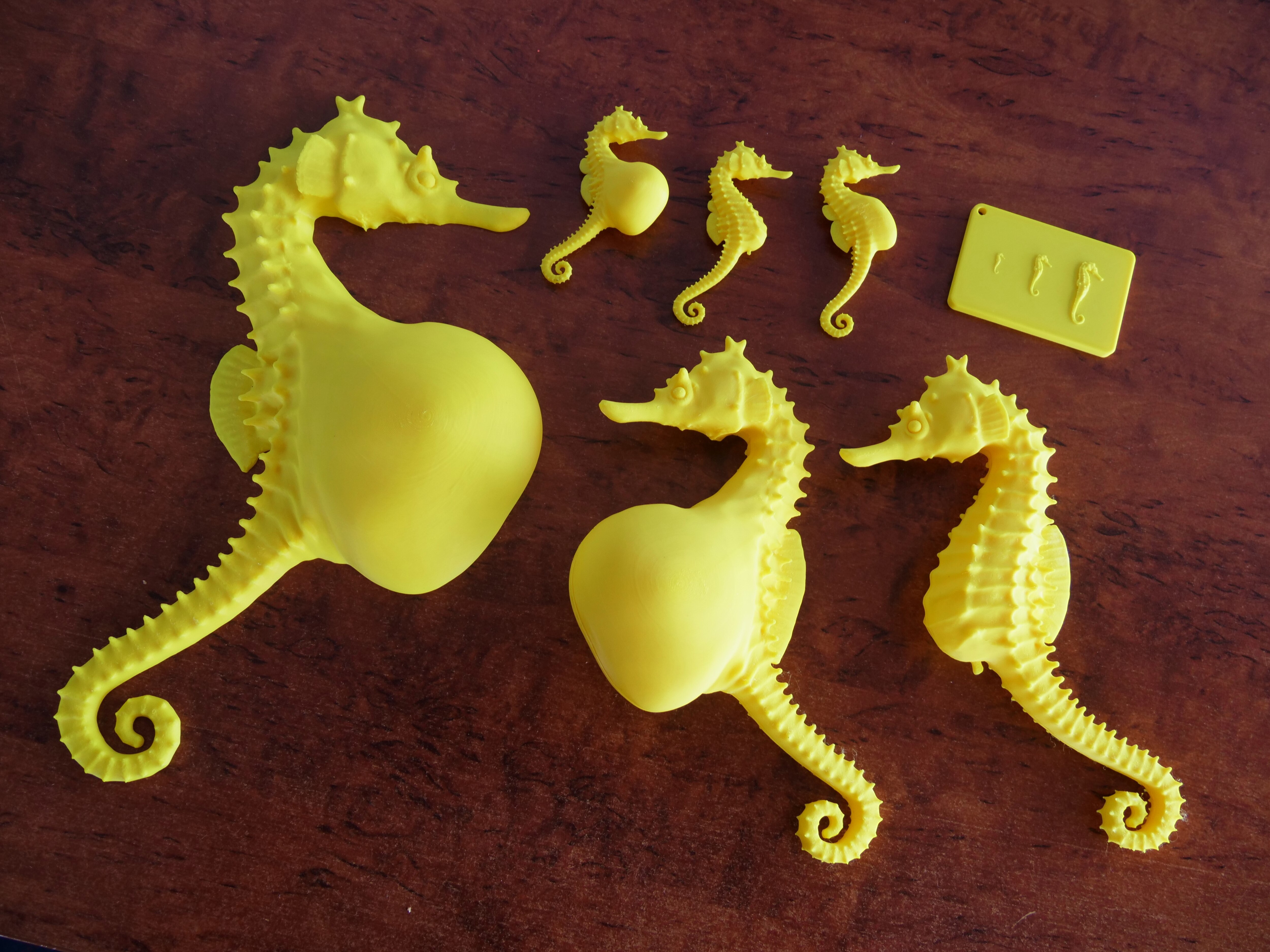 Seven small yellow 3D printed animated seahorses laid out on a wooden desk.