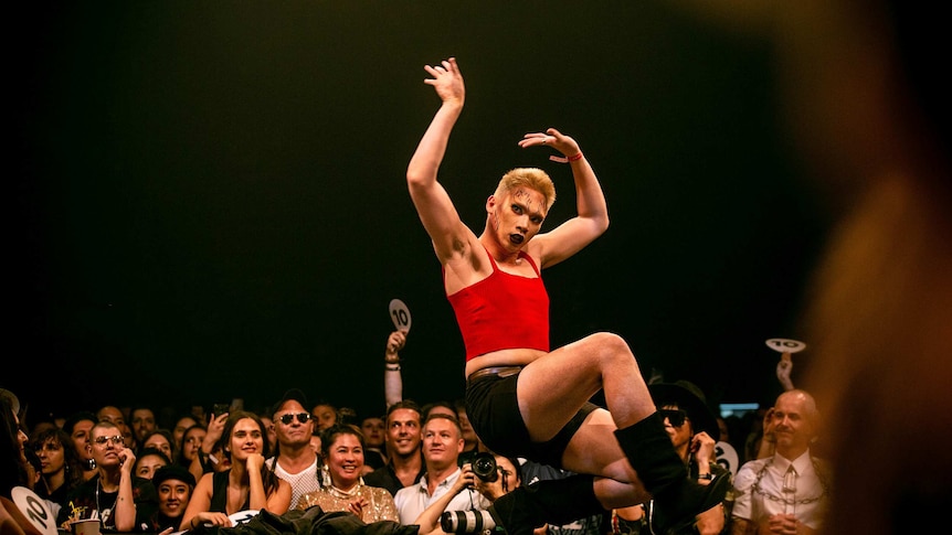 A vogue performer in a red shirt and dramatic makeup in the middle of a move on the runway at Sissy Ball 2019.