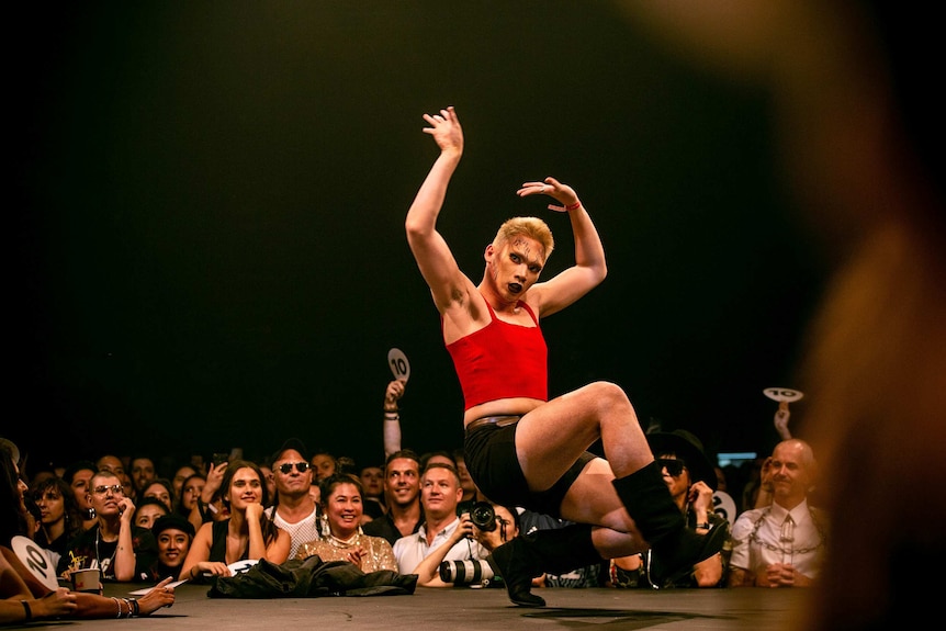 A vogue performer in a red shirt and dramatic makeup in the middle of a move on the runway at Sissy Ball 2019.