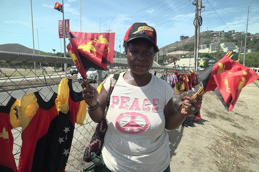 Street vendor in Port Moresby holds up flags for sale at a market.