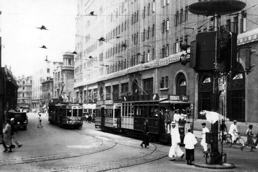 A 1930s black and white photo of a busy city street with trams, bikes and people