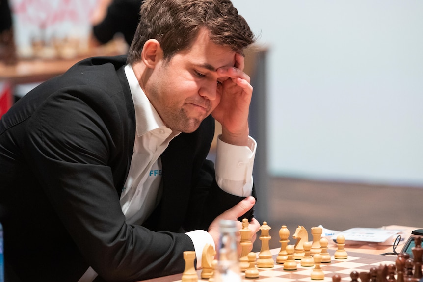 A man in a suit looks pensively at a chess board