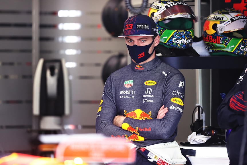 Max Verstappen stands with his arms folded wearing a mask