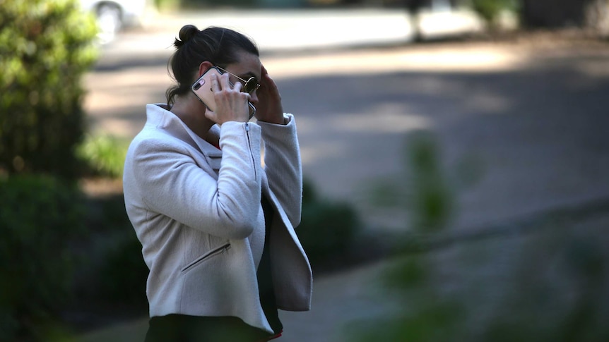 Photo of a woman holding a mobile phone, her hand up to her forehead.