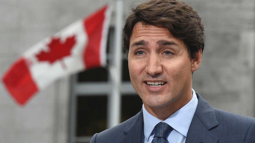 Justin Trudeau stands in front of a Canadian flag.