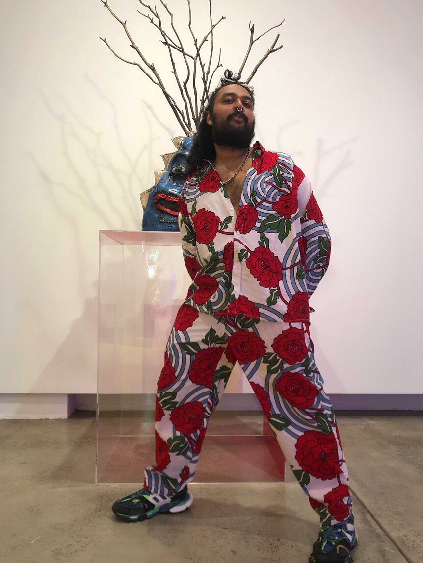 Man in suit patterned with red flowers stands in front of a sculpture.