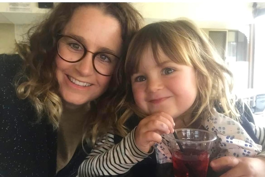 Close up of mum in glasses and small girl with drink both looking at camera 
