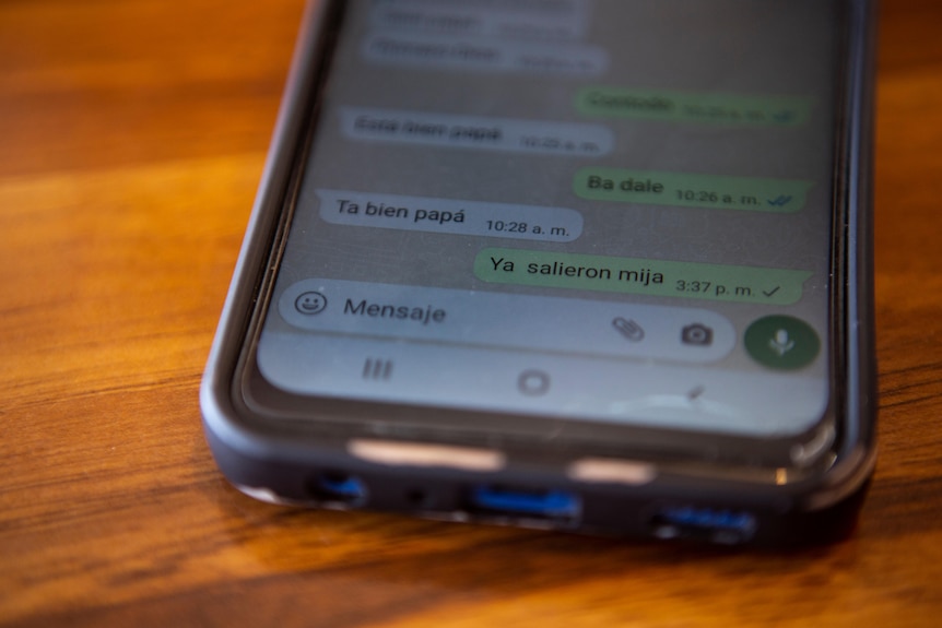 A photo of a phone resting on a wooden table showing two-way text messages on the WhatsApp app 