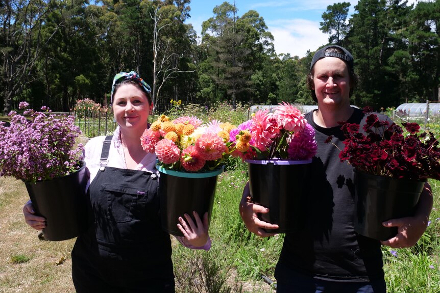 A couple hold buckets of flowers and smile