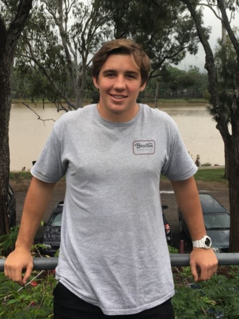 young man in t shirt in front of trees and river