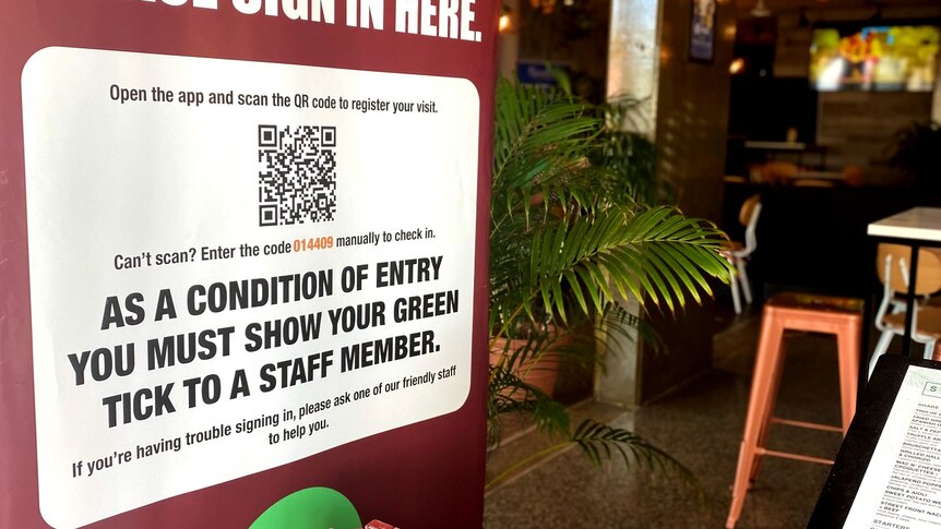 A poster of a restaurant's QR Code is outside of a restaurant, a green bush behind it. 