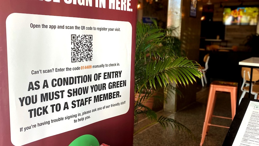 A poster of a restaurant's QR Code is outside of a restaurant, a green bush behind it. 