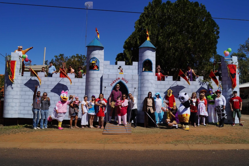 A large group of people stand outside a large castle cut-out.