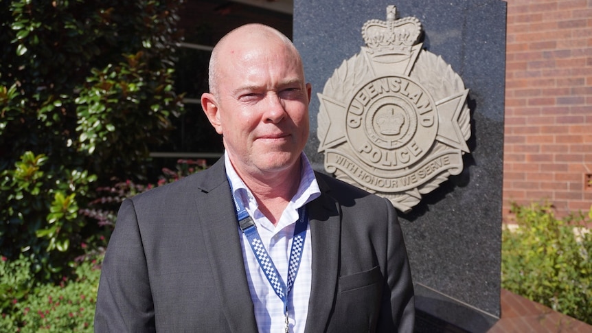 A man standing in front of a Queensland Police Service logo