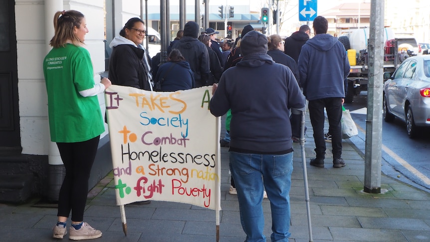 A woman and a man holding a sign between them, which reads, It takes a society to combat homelessness 