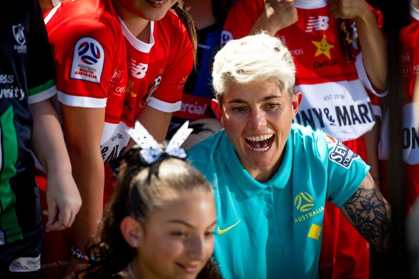 A woman with short blonde hair surrounded by footballers 